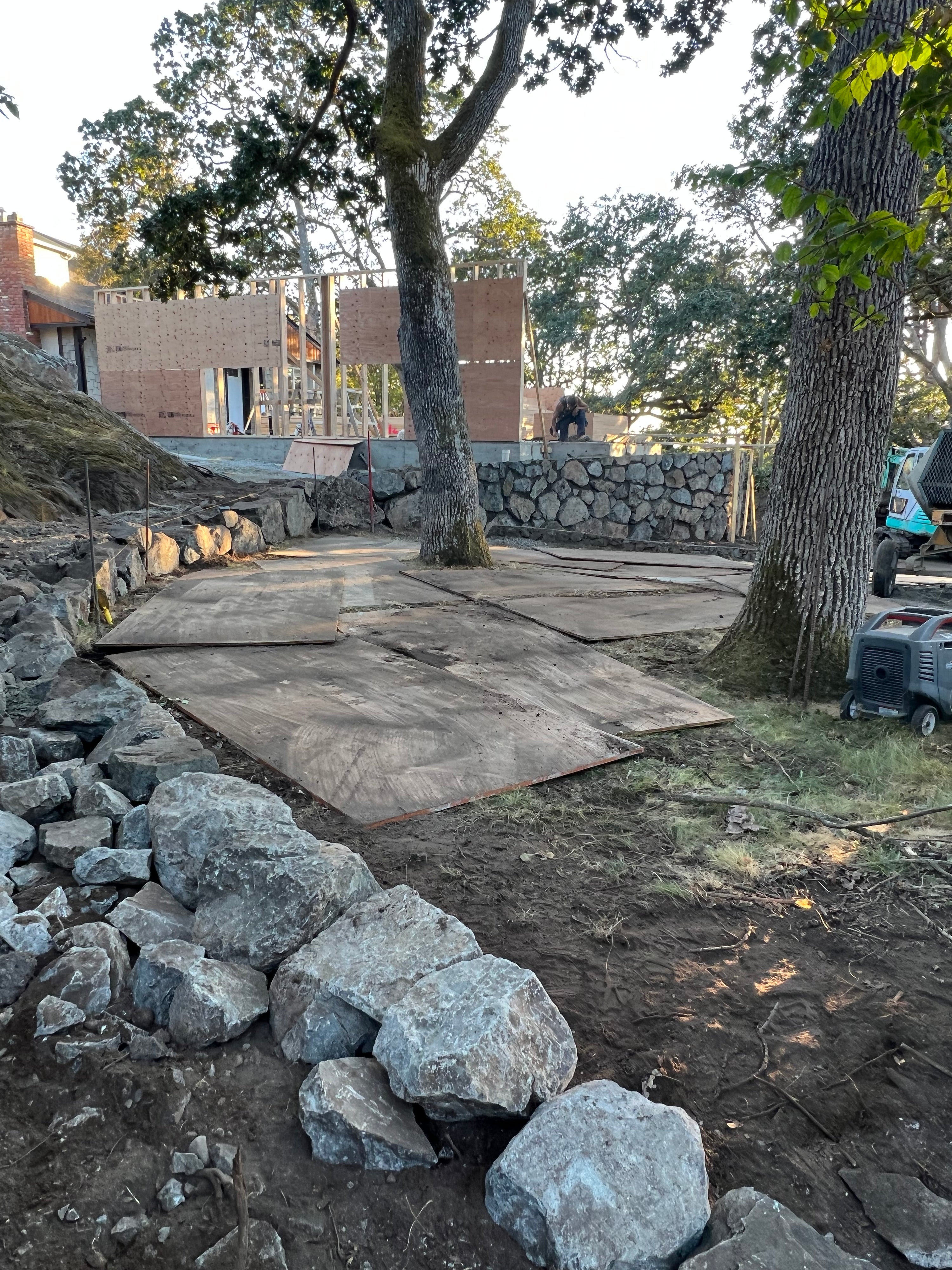 House framing set in oak trees with rock walk way